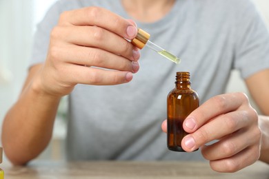 Young man dripping CBD tincture into bottle from dropper at wooden table, closeup