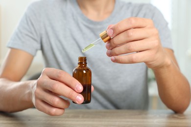 Photo of Young man dripping CBD tincture into bottle from dropper at wooden table, closeup