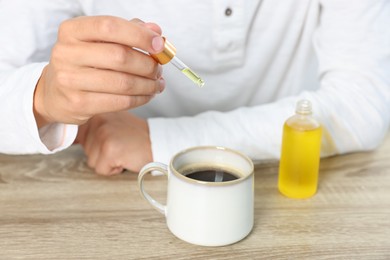 Photo of Young man dripping CBD tincture into drink at wooden table, closeup