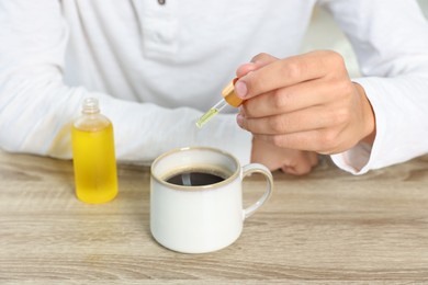 Photo of Young man dripping CBD tincture into drink at wooden table, closeup