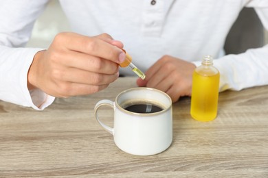 Young man dripping CBD tincture into drink at wooden table, closeup