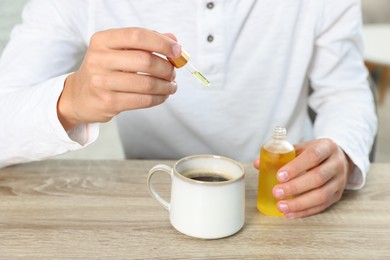 Photo of Young man dripping CBD tincture into drink at wooden table, closeup