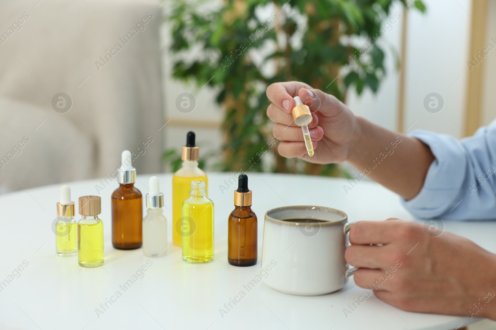 Photo of Young man dripping CBD tincture into drink at white table, closeup