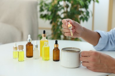 Young man dripping CBD tincture into drink at white table, closeup