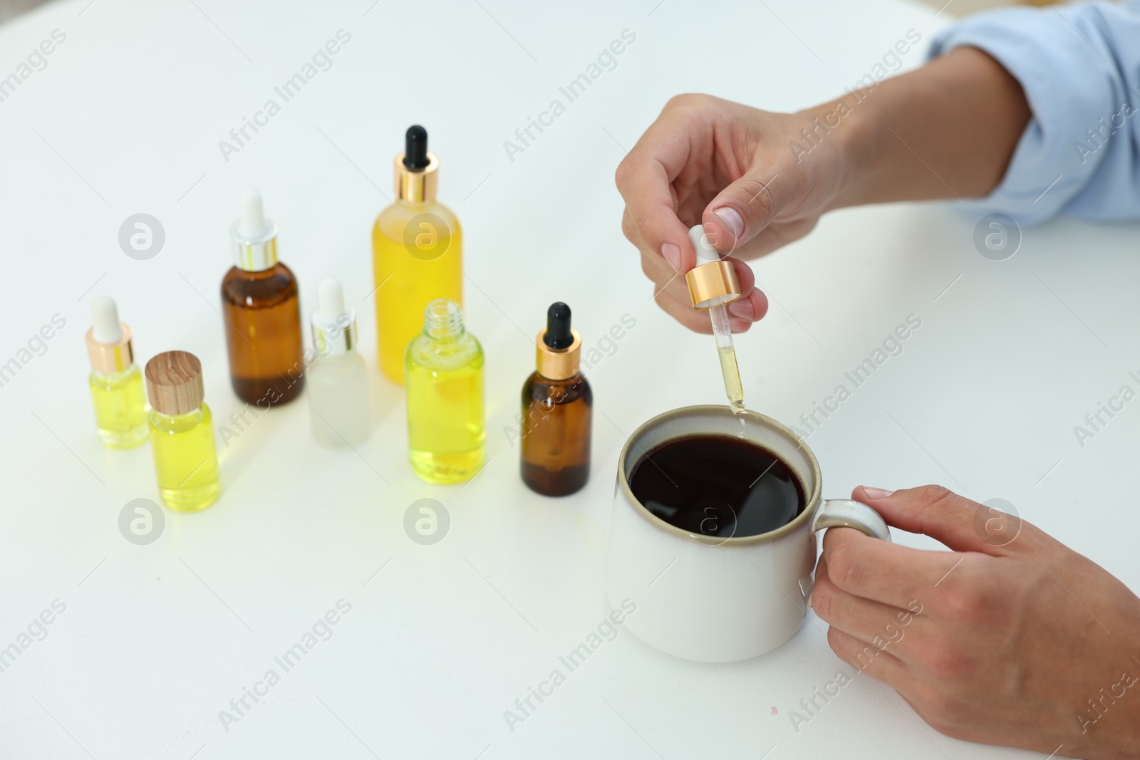 Photo of Young man dripping CBD tincture into drink at white table, closeup