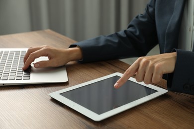 Photo of Businesswoman using laptop and tablet at wooden table indoors, closeup. Modern technology