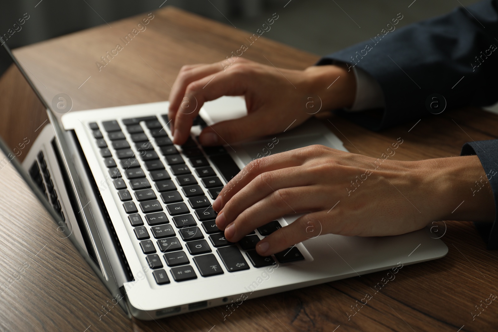 Photo of Businesswoman using laptop at wooden table indoors, closeup. Modern technology