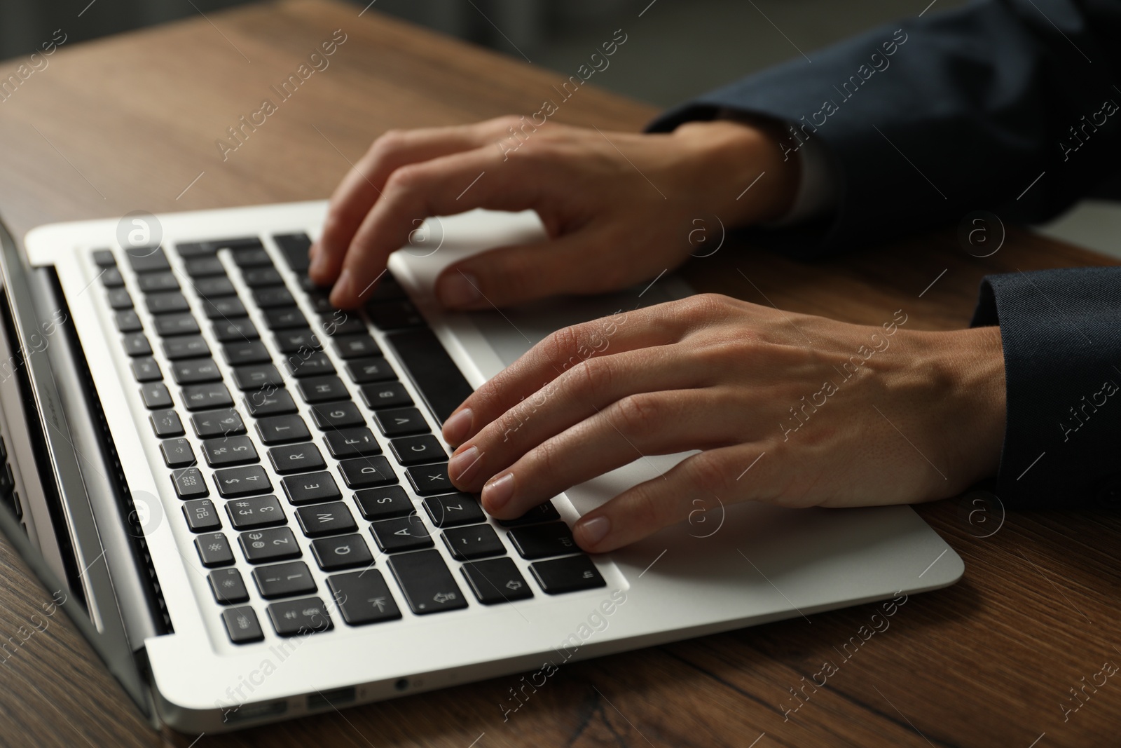 Photo of Businesswoman using laptop at wooden table indoors, closeup. Modern technology