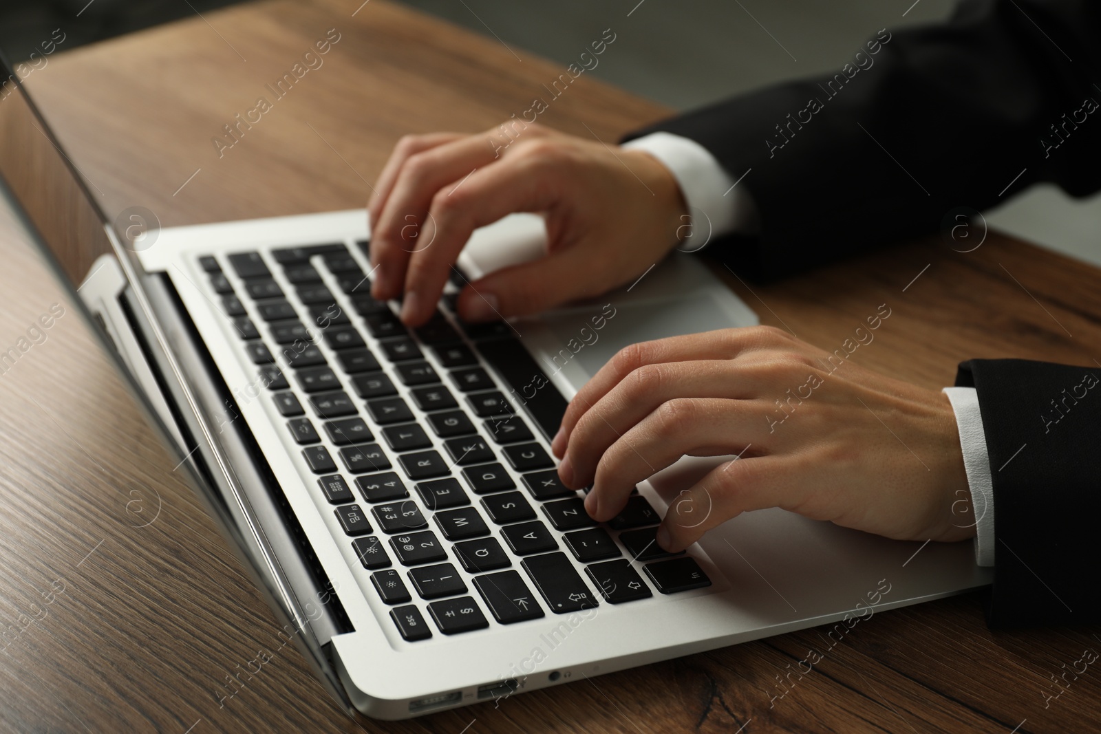 Photo of Businesswoman using laptop at wooden table indoors, closeup. Modern technology