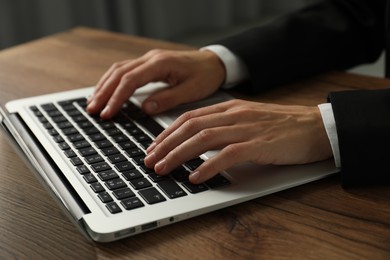 Photo of Businesswoman using laptop at wooden table indoors, closeup. Modern technology