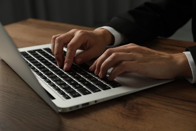 Photo of Businesswoman using laptop at wooden table indoors, closeup. Modern technology