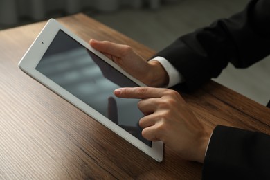 Photo of Businesswoman using tablet at wooden table indoors, closeup. Modern technology