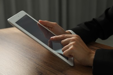 Photo of Businesswoman using tablet at wooden table indoors, closeup. Modern technology