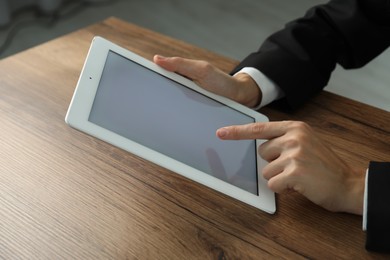 Photo of Businesswoman using tablet at wooden table indoors, closeup. Modern technology