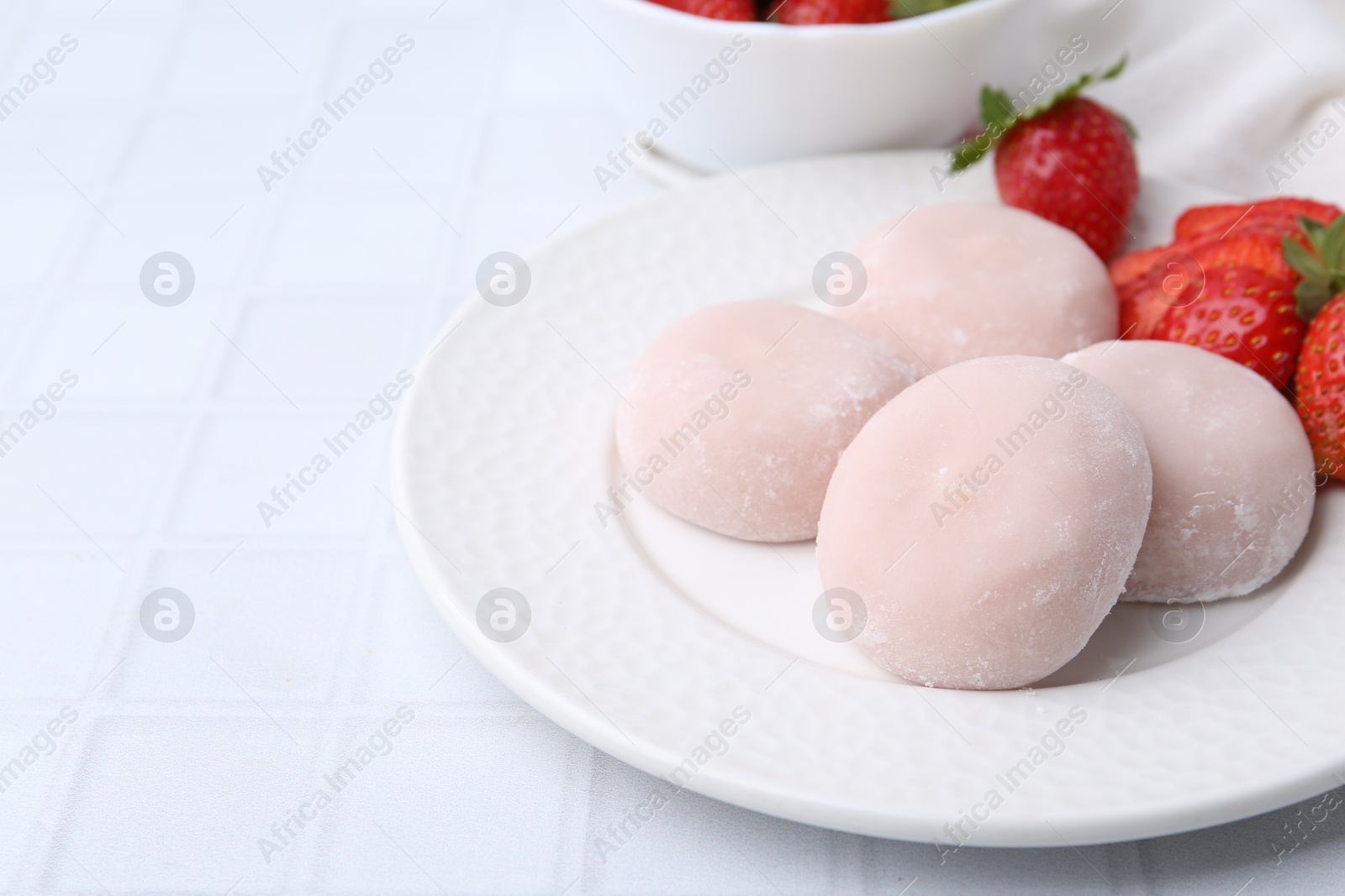 Photo of Delicious mochi and strawberries on white tiled table, closeup