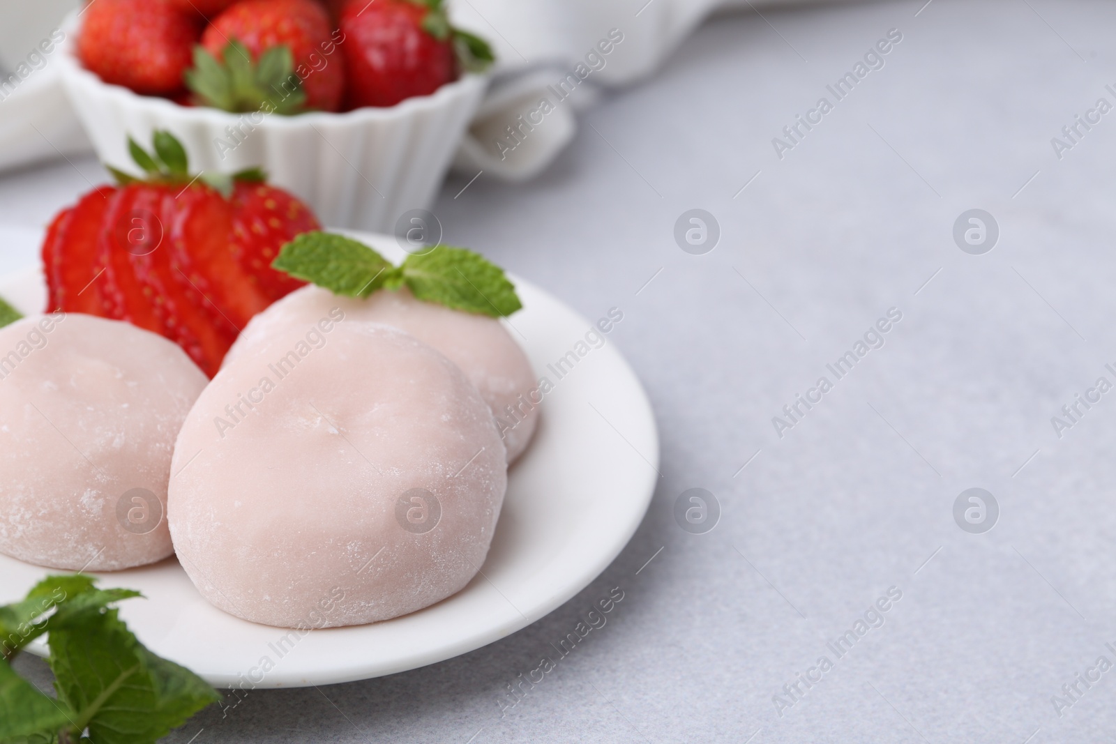 Photo of Delicious mochi, strawberries and mint on light grey table, closeup. Space for text