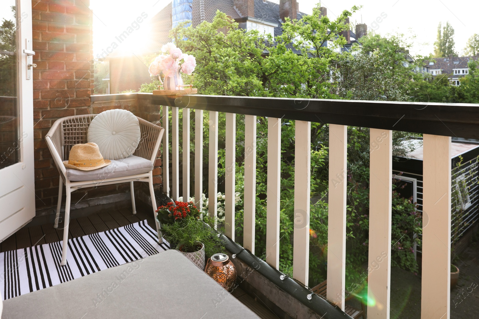 Photo of Vase with beautiful peonies on railings and chair at cozy balcony on sunny day