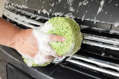 Man washing car hood with sponge indoors, closeup