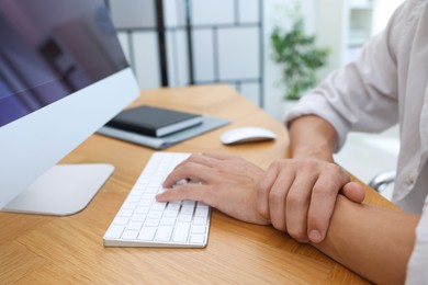 Photo of Man suffering from pain in wrist while working on computer at table indoors, closeup. Carpal tunnel syndrome