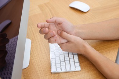 Photo of Man suffering from pain in wrist while working on computer at wooden table, closeup. Carpal tunnel syndrome