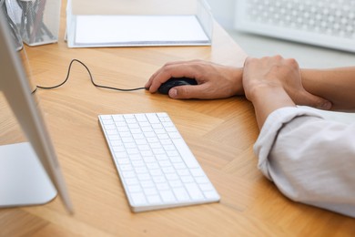 Photo of Man suffering from pain in wrist while using computer mouse at table indoors, closeup. Carpal tunnel syndrome