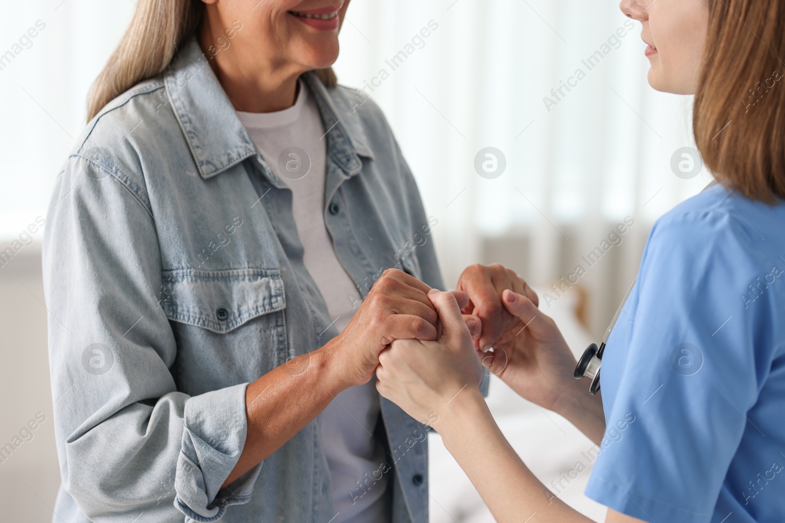 Photo of Young healthcare worker supporting senior patient indoors, closeup