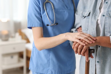 Photo of Young healthcare worker supporting senior patient indoors, closeup