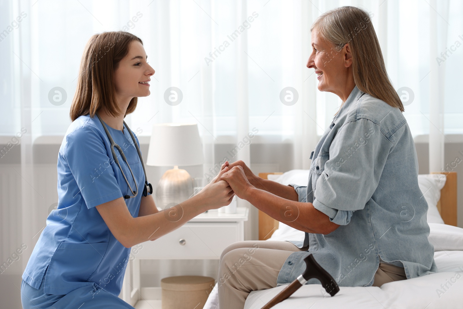 Photo of Smiling healthcare worker supporting senior patient indoors