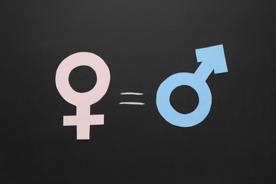 Photo of Equals sign between female and male gender symbols on chalkboard, flat lay