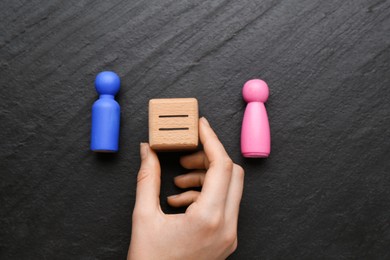 Photo of Gender equality concept. Woman holding wooden cube with equals sign between female and male figures at grey textured background, top view