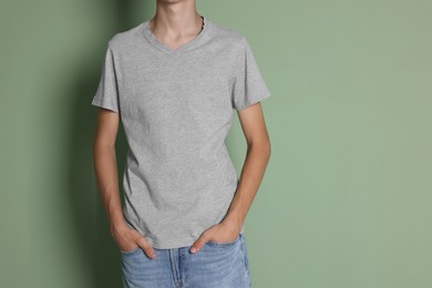 Photo of Teenage boy wearing light grey t-shirt on green background, closeup. Space for text