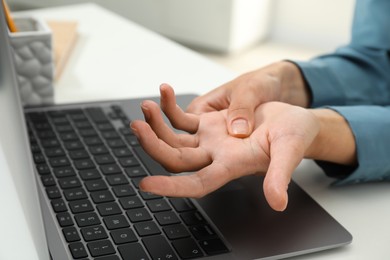 Photo of Carpal tunnel syndrome. Woman suffering from pain in wrist at desk indoors, closeup