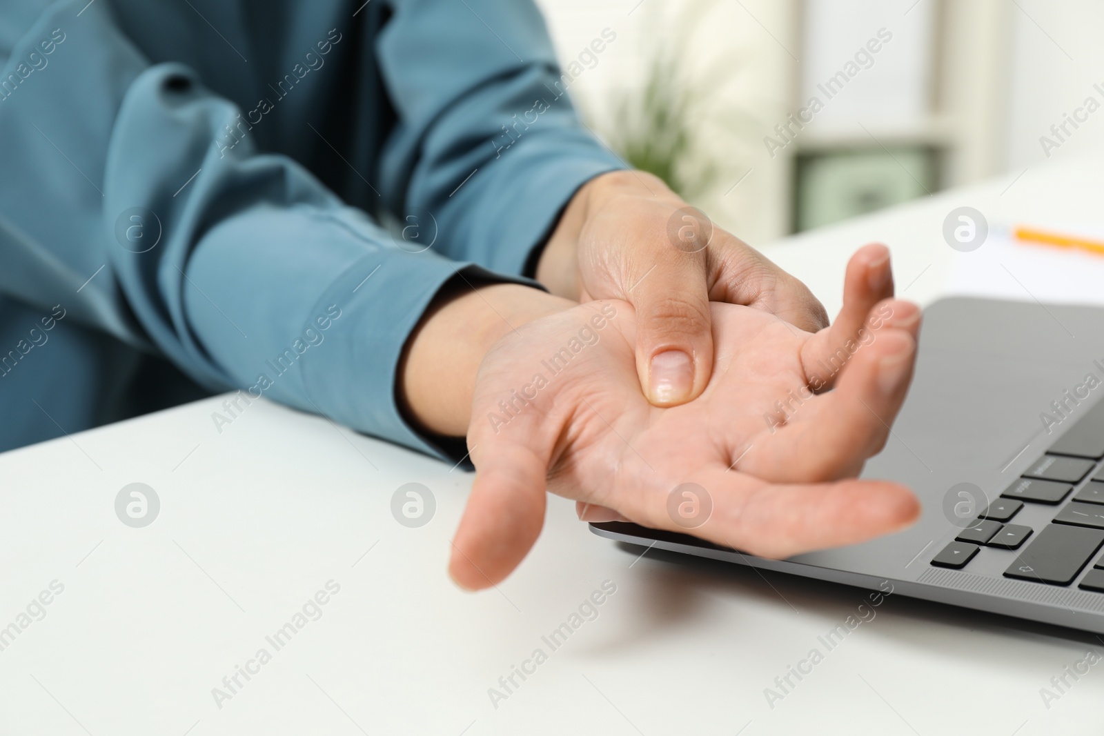 Photo of Carpal tunnel syndrome. Woman suffering from pain in wrist at desk indoors, closeup