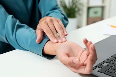 Photo of Carpal tunnel syndrome. Woman suffering from pain in wrist at desk indoors, closeup