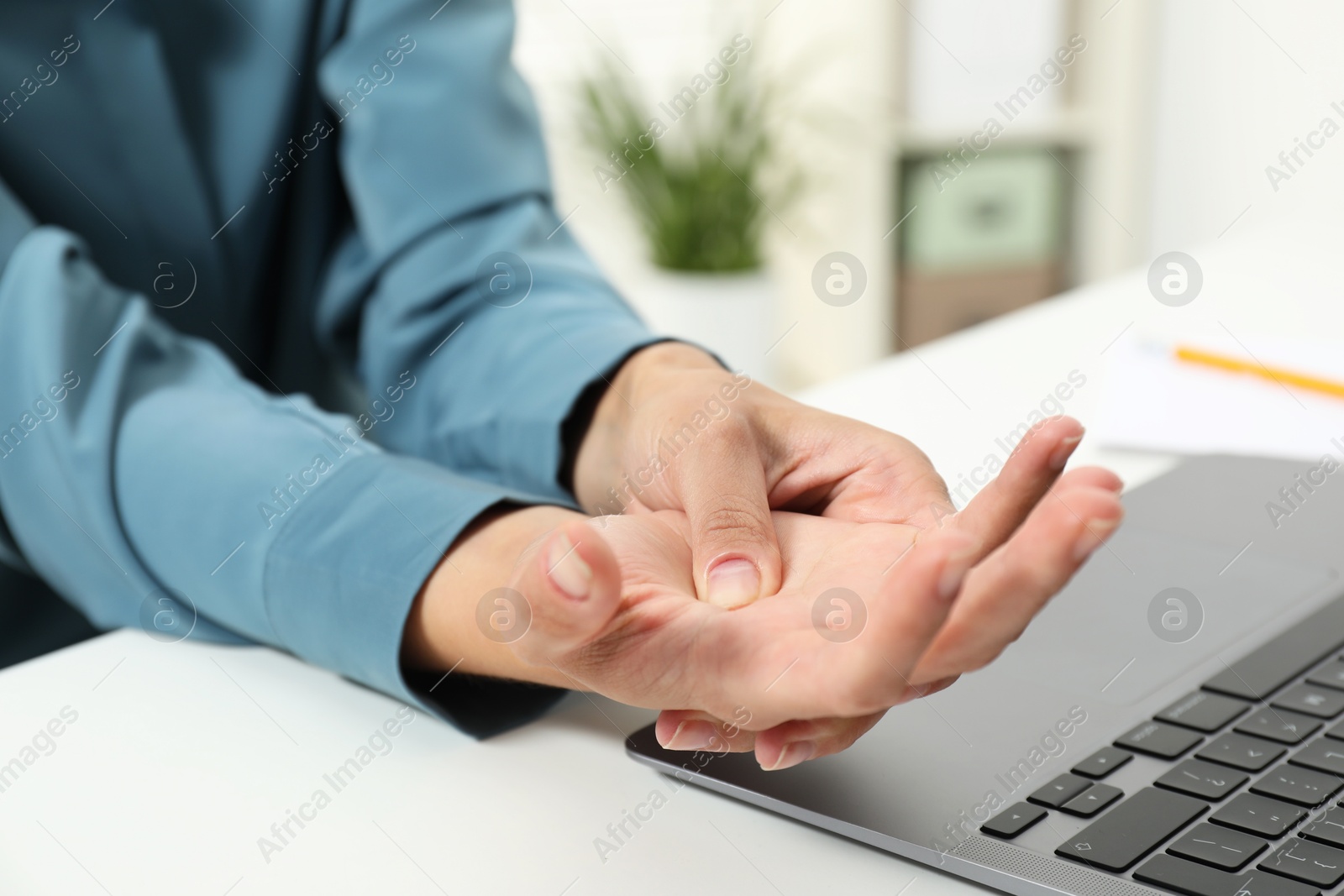 Photo of Carpal tunnel syndrome. Woman suffering from pain in wrist at desk indoors, closeup