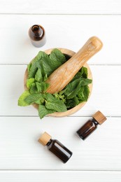 Photo of Tinctures in bottles, mortar, pestle and mint on white wooden table, flat lay