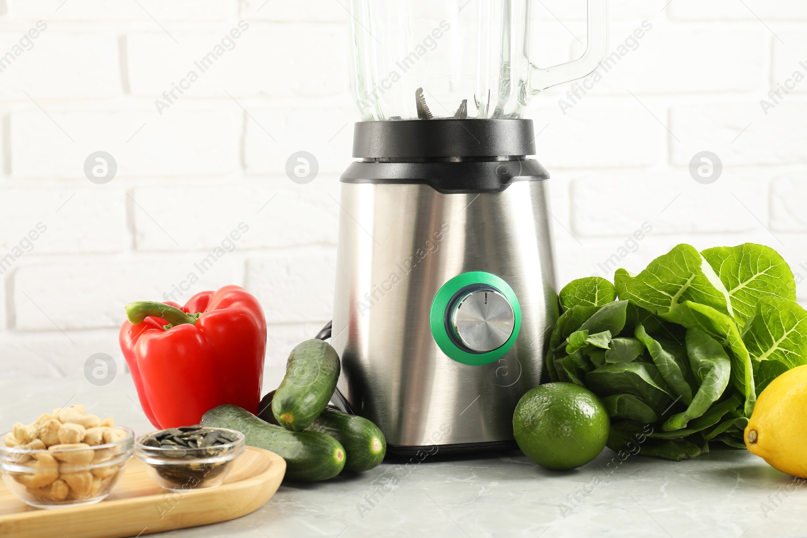 Photo of Blender and products on light table against white brick wall