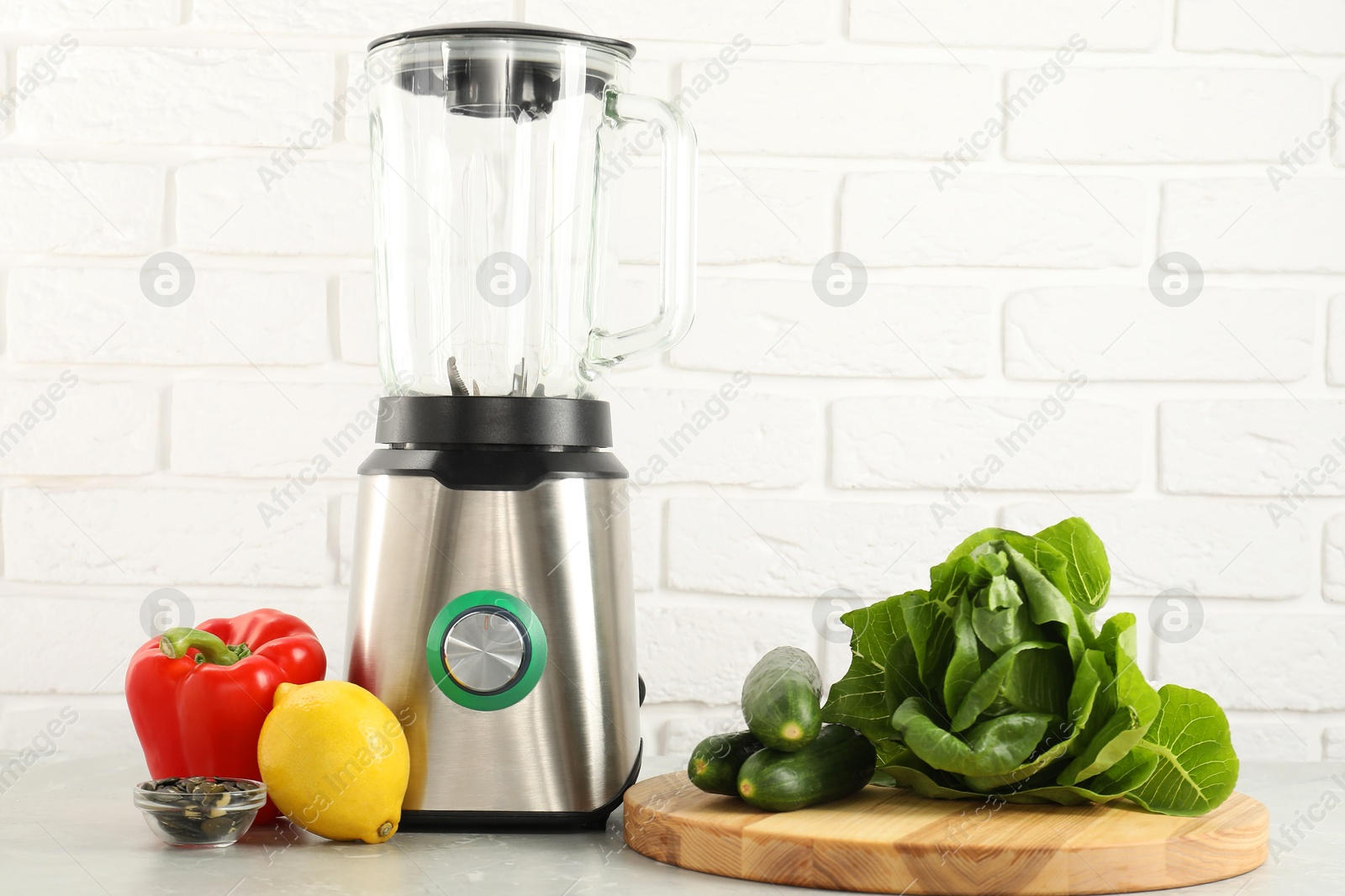 Photo of Blender and products on light table against white brick wall