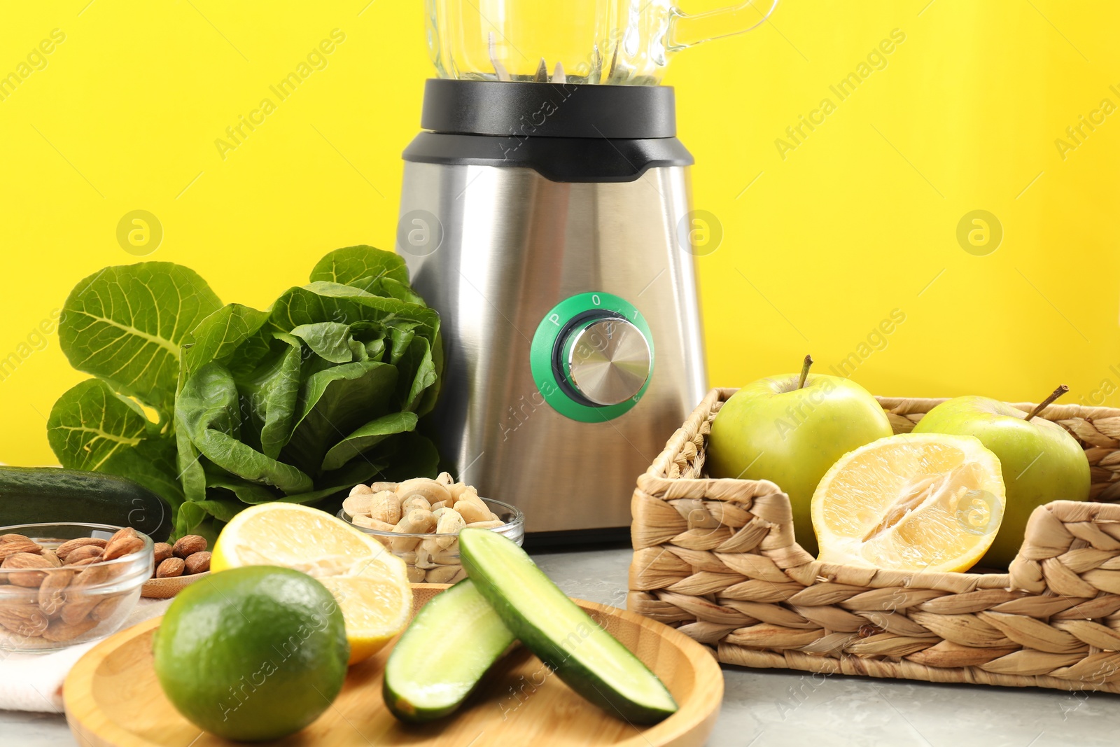 Photo of Blender and products on grey table against yellow background, closeup