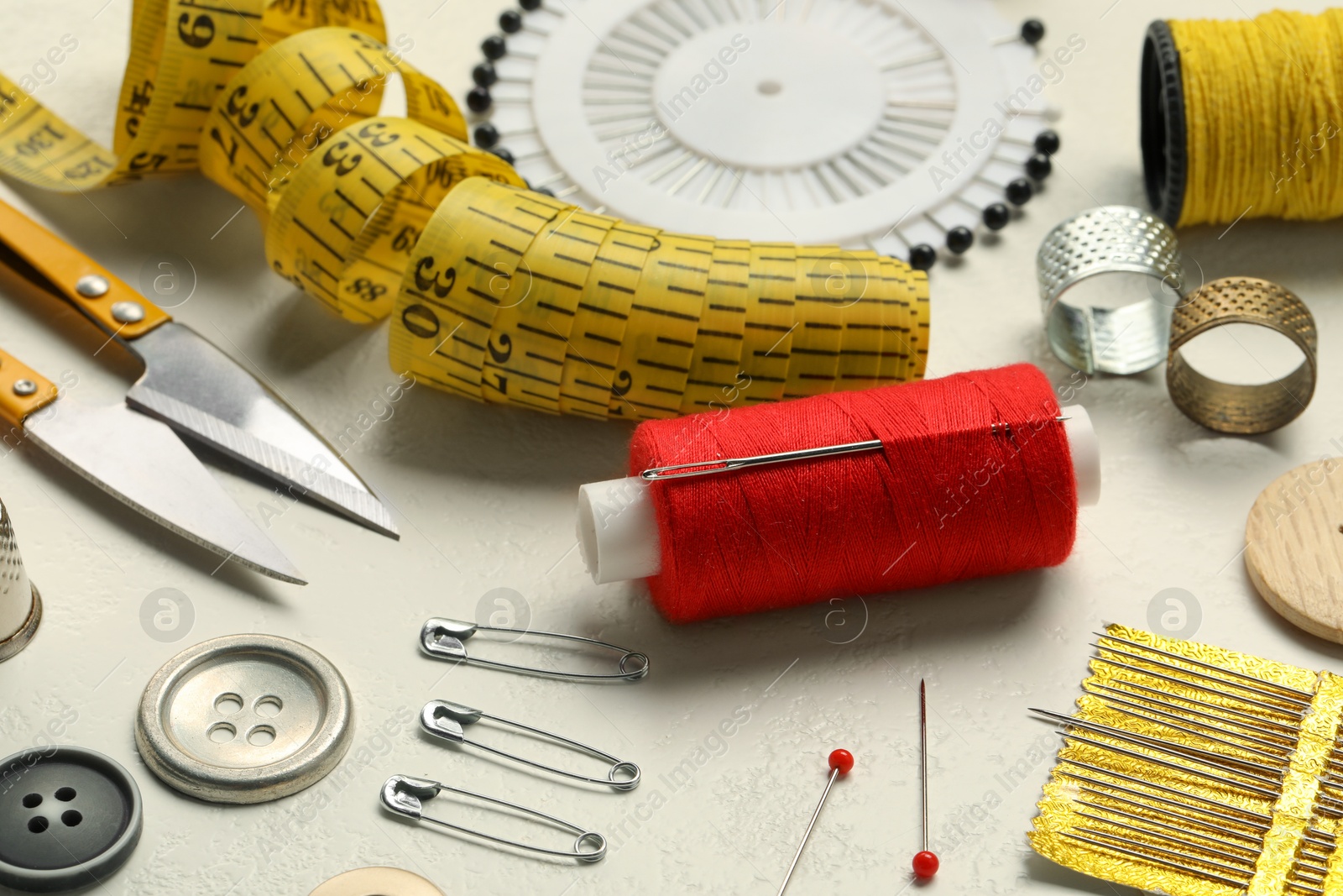 Photo of Different sewing tools on white textured table, closeup