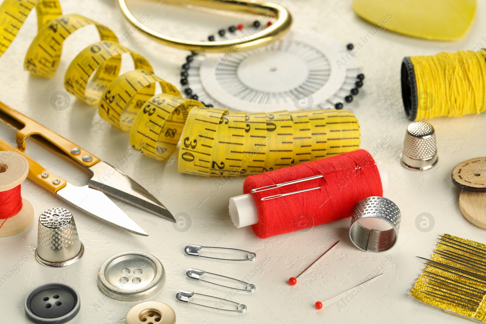 Photo of Different sewing tools on white textured table, closeup