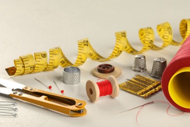 Photo of Different sewing tools on white textured table, closeup