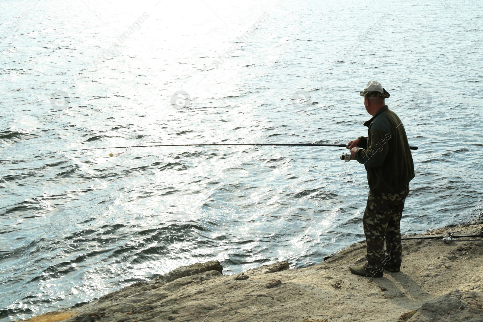 Photo of Fisherman with rod fishing near lake at summer, back view