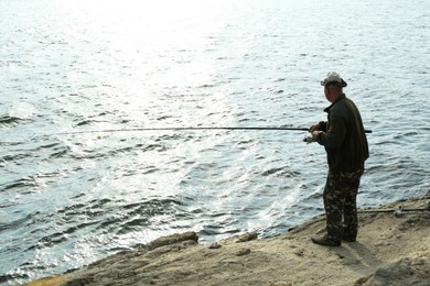 Fisherman with rod fishing near lake at summer, back view