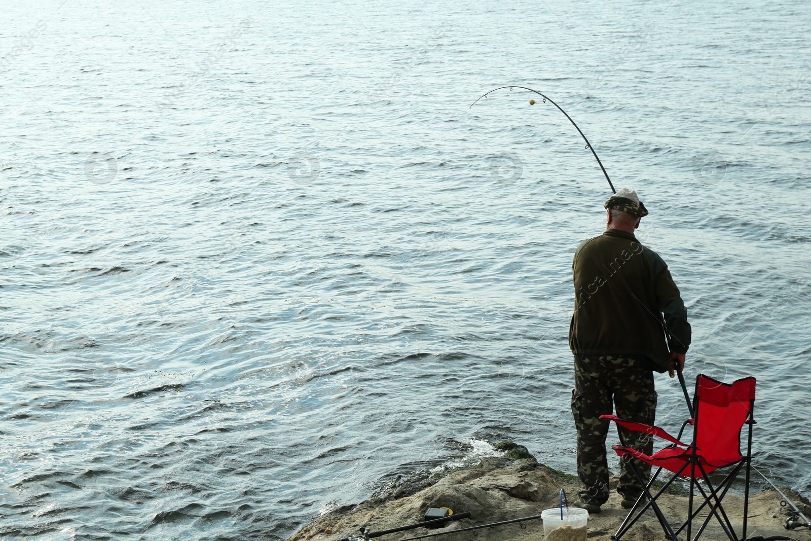 Photo of Fisherman with rod fishing near lake at summer, back view. Space for text