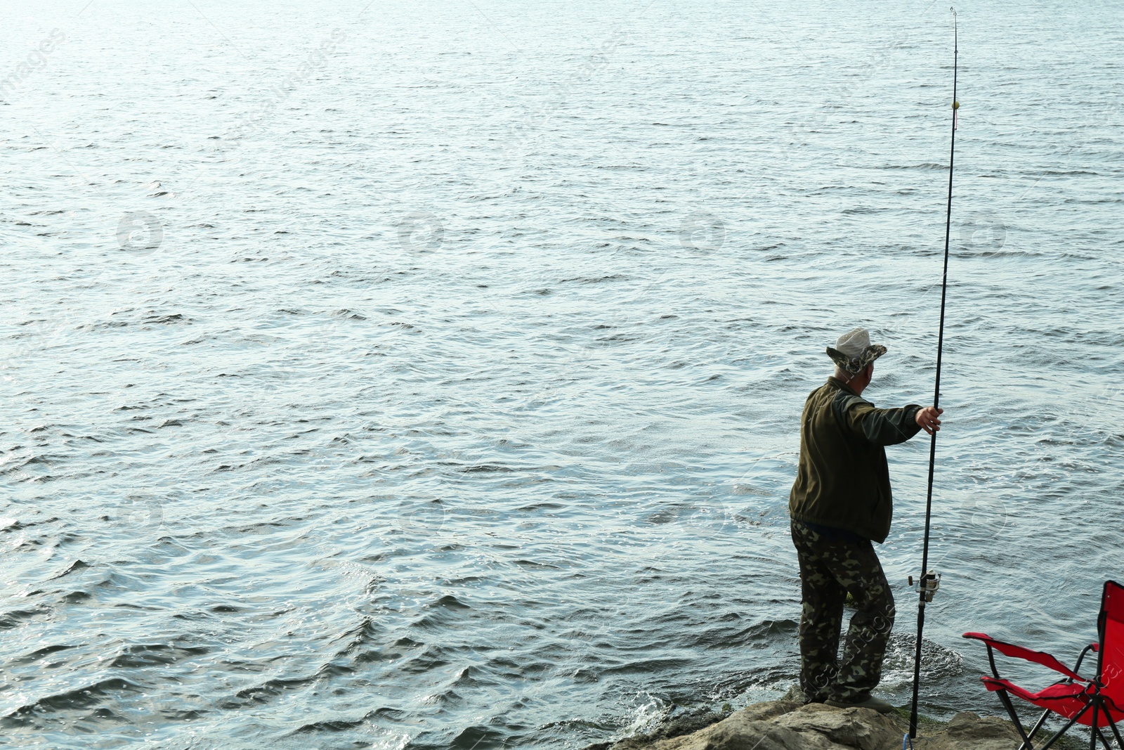 Photo of Fisherman with rod fishing near lake at summer, back view. Space for text