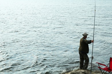 Fisherman with rod fishing near lake at summer, back view. Space for text