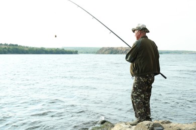 Photo of Fisherman with rod fishing near lake at summer, back view. Space for text