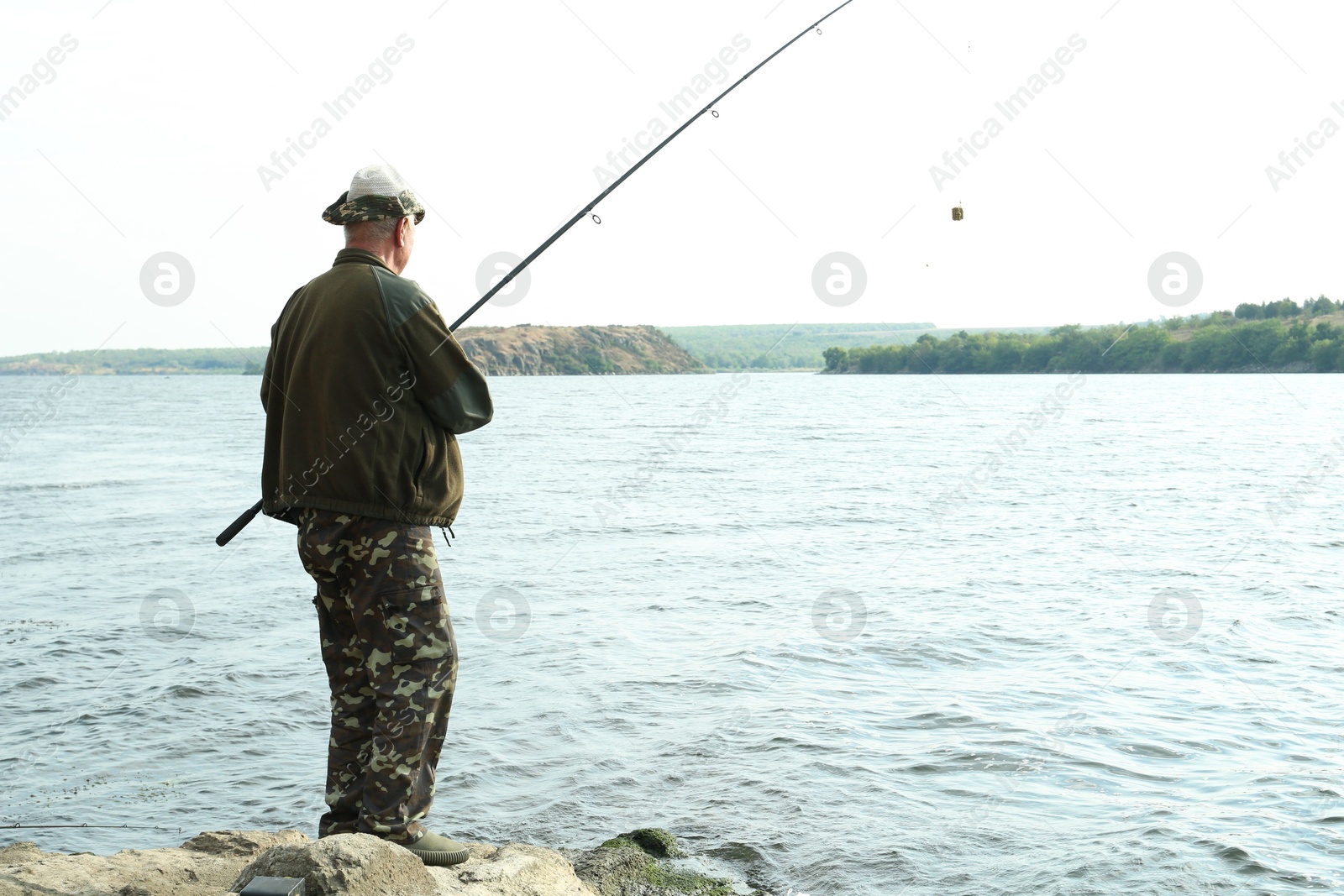 Photo of Fisherman with rod fishing near lake at summer, back view. Space for text