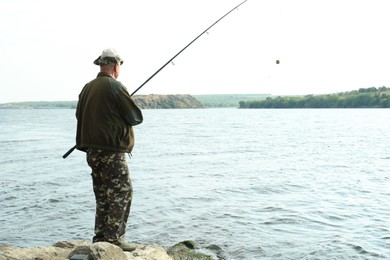 Photo of Fisherman with rod fishing near lake at summer, back view. Space for text